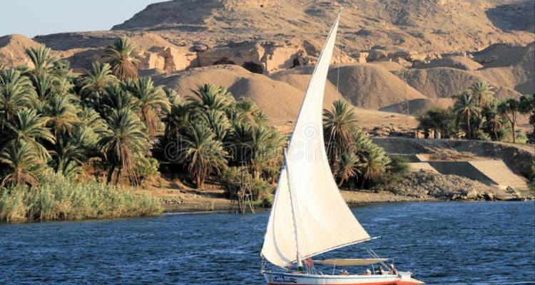 Barco de vela tradicional en el río Nilo contra un fondo desértico.