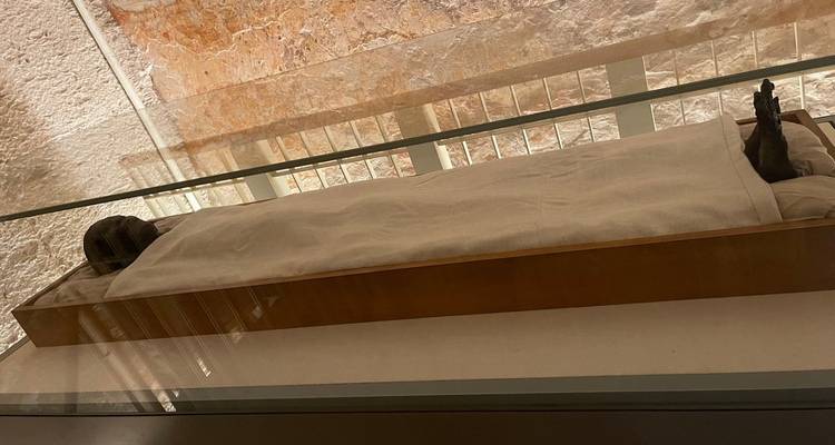 Momia en exhibición en un museo con vidrio reflectante.