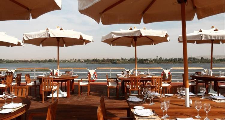 Speisebereich am Flussufer mit Tischen und Sonnenschirmen mit Blick auf den Nil.