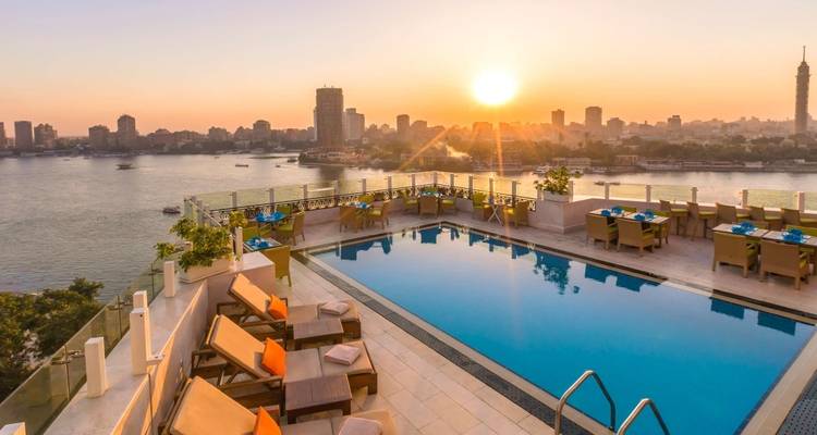 Dakzwembad met uitzicht op een rivier en stadsskyline bij zonsondergang.