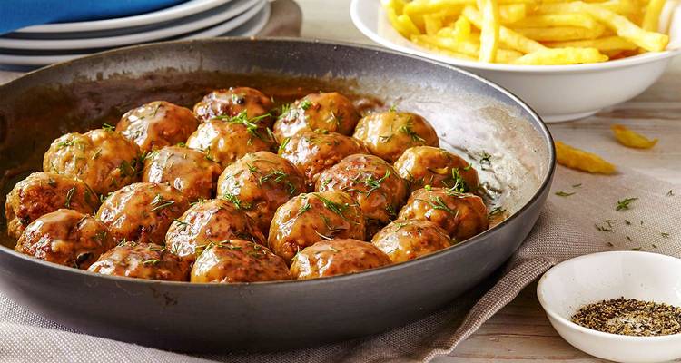 A pan of Swedish meatballs in gravy with fries in the background.