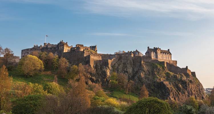 View of Edinburgh Castle atop a rocky hill with trees below.