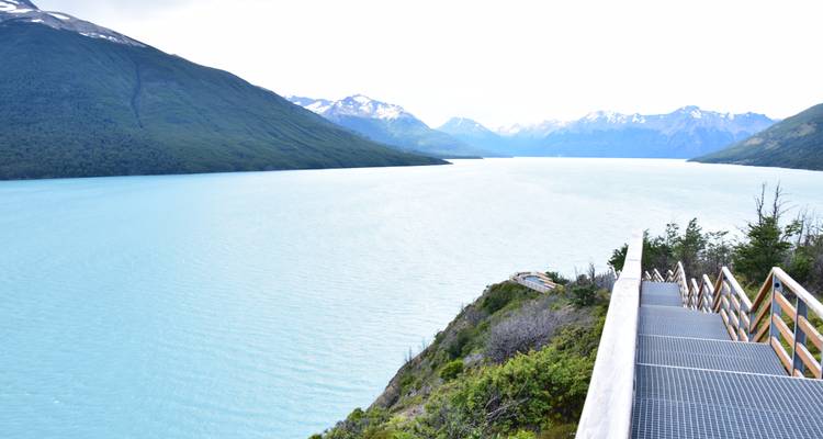Aussichtsplattform mit Blick auf einen großen, ruhigen blauen See umgeben von Bergen.