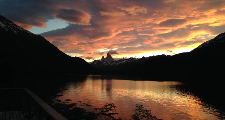Dramatischer Sonnenuntergangshimmel über einem von Bergen umgebenen See.