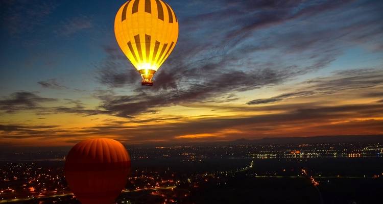 Heißluftballons, die bei Abenddämmerung über eine Landschaft schweben.