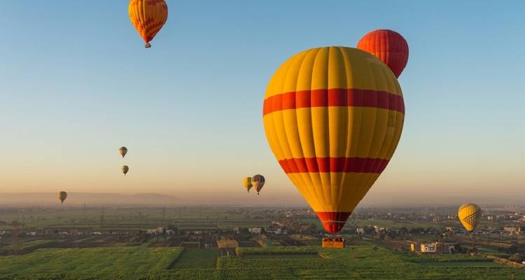 Heteluchtballonnen die bij zonsopgang over landbouwgrond vliegen.