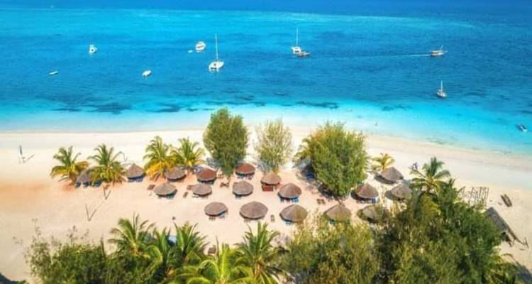 Luftaufnahme eines Strandes mit Sonnenschirmen und klarem azurblauem Wasser.