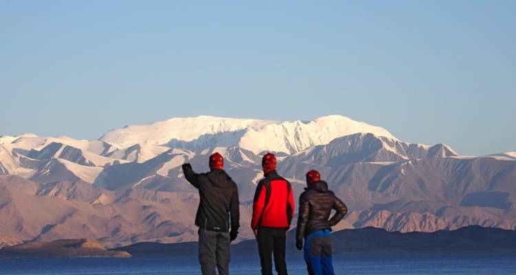 People admiring snowy mountains by a lake.