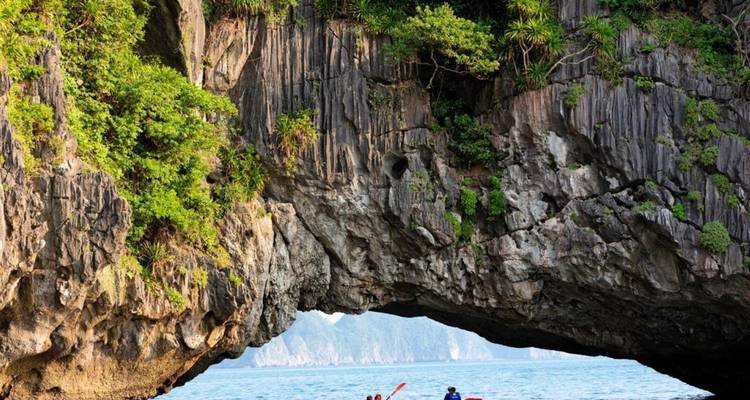 Kajakfahrer unter einer dramatischen natürlichen Bogenformation mit üppigem Grün.