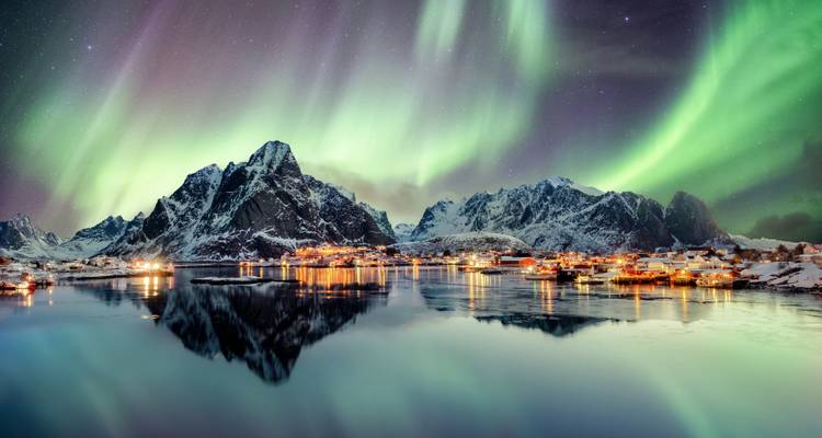 Aurores boréales au-dessus d'un village de fjord avec des sommets enneigés.