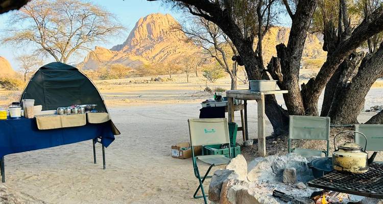 Installation de camping sous une formation rocheuse dans un paysage désertique en Namibie.