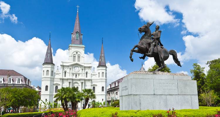 Historic church with statue in the foreground under a bright blue sky.