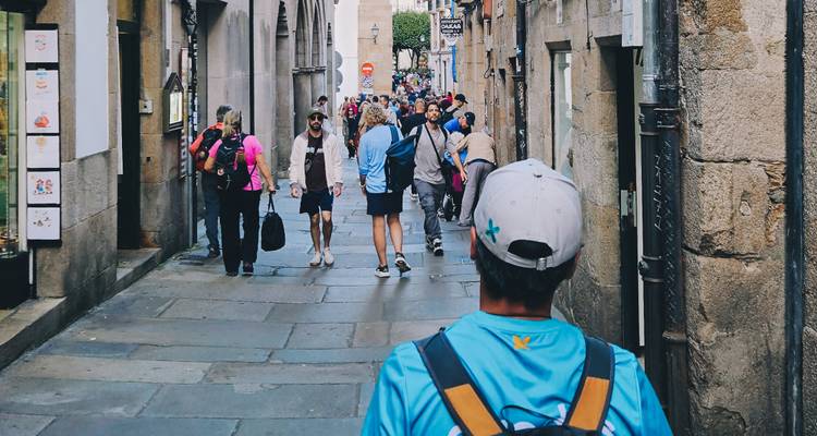 Peregrinos y turistas caminando por una concurrida calle antigua de piedra en la ruta del Camino.