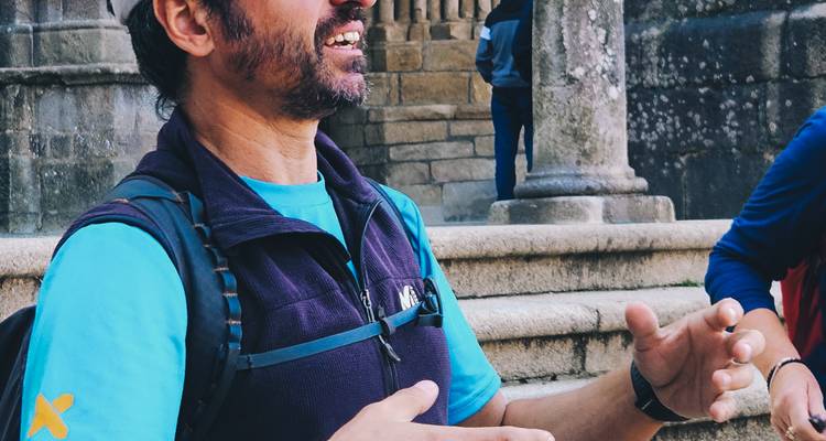 Primer plano de un guía de trekking hablando con entusiasmo fuera de una arquitectura de piedra histórica.