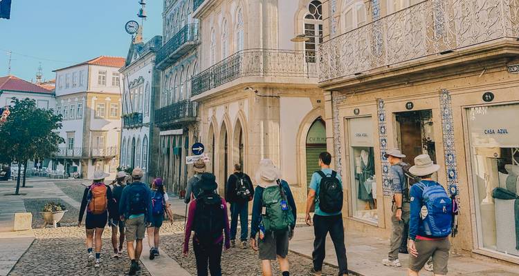 Excursionistas con mochilas explorando un encantador pueblo portugués con fachadas de azulejos.