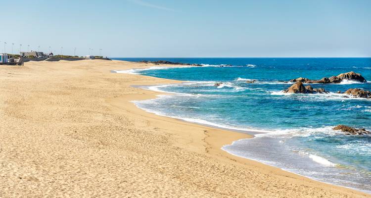 Plage de sable fin avec des vagues douces et des eaux turquoise de l'Atlantique sous un ciel bleu clair.