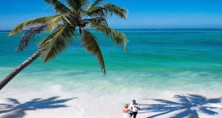 Ein Paar an einem tropischen Strand mit klarem blauem Wasser und Palmenschatten.