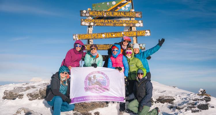 Groupe de grimpeurs enthousiastes posant près du panneau iconique d'Uhuru Peak au sommet du Mont Kilimandjaro couvert de neige.