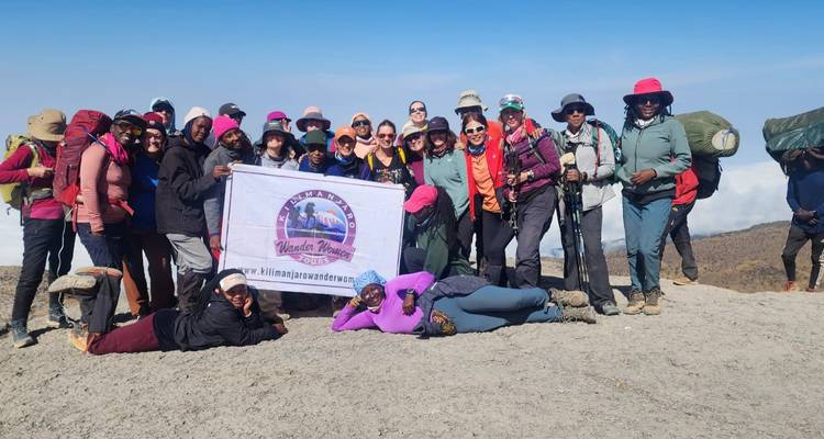 Grand groupe de randonneurs posant sur un versant volcanique aride tenant une bannière d'aventure du Kilimandjaro