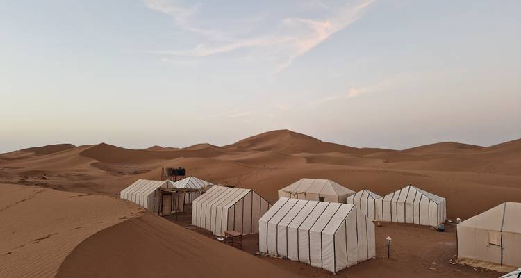 Un campement dans le désert avec des tentes installées au milieu des dunes de sable.