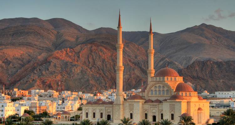 Grande mosquée aux deux minarets situés contre des montagnes accidentées à la lumière du coucher de soleil.