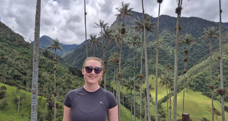 Smiling woman in sportswear and sunglasses posing in front of towering wax palm trees and verdant mountains