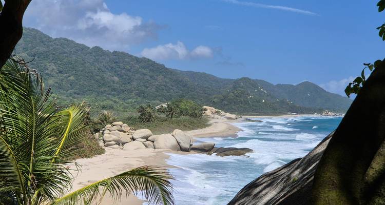 Pristine tropical beach with jungle-covered hills, large boulders and turquoise waves under a clear blue sky