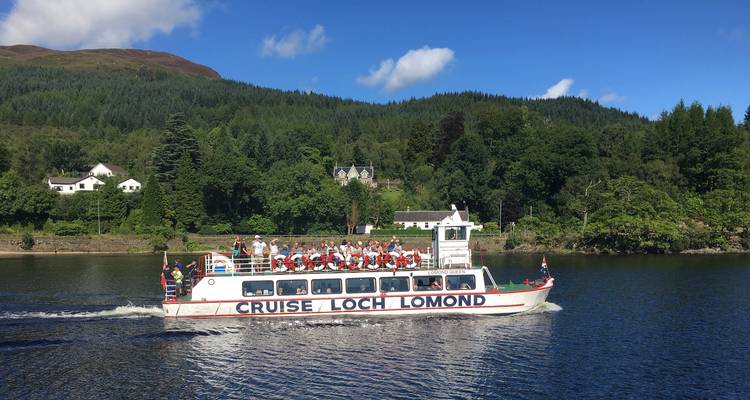 Barco turístico navegando por un gran lago rodeado de colinas y árboles.