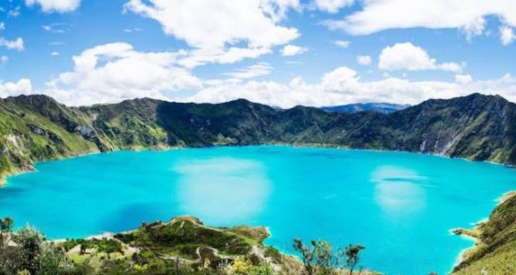 Expansive view of a vibrant blue crater lake surrounded by mountains.
