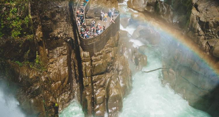 Stairs carved into rock next to a powerful waterfall with rainbow.