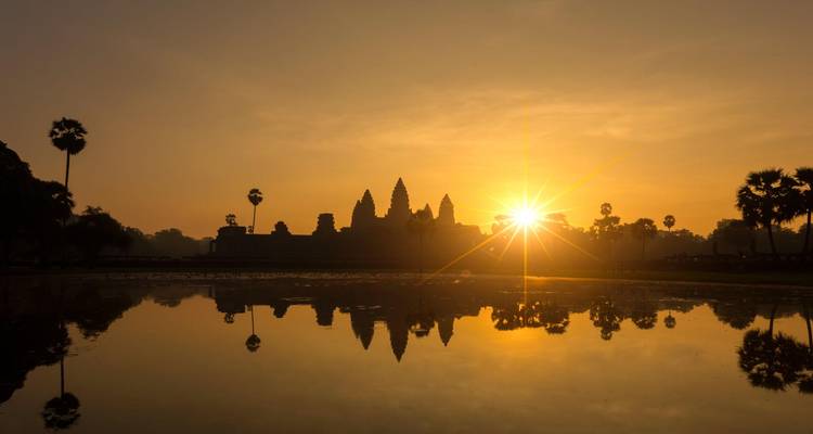 Amanecer dorado detrás de la silueta de las torres de Angkor Wat reflejado en una piscina de agua quieta.
