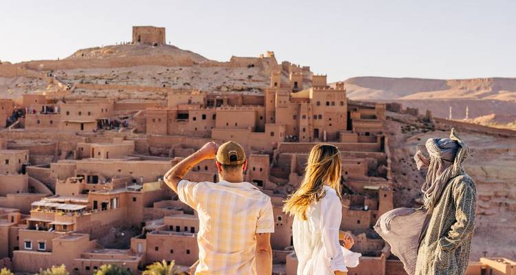 Reizigers bewonderen het versterkte kleidorp Ait Benhaddou vanaf een winderig uitzichtspunt.