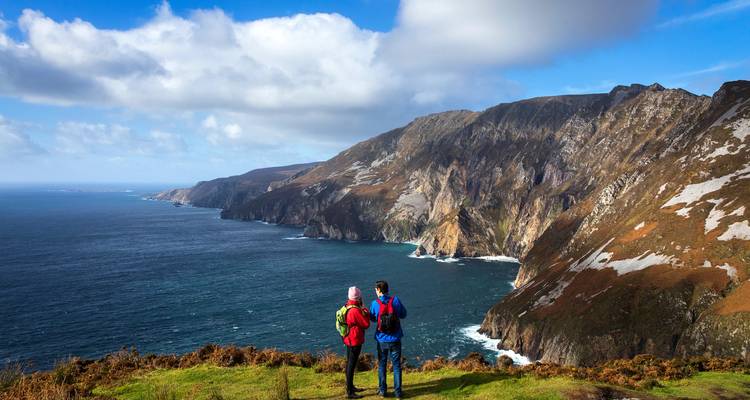 Two people looking out over a coastal cliff landscape.