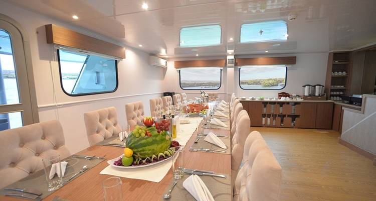 Mesa de comedor elegante a bordo decorada con un centro de frutas, servilletas y vistas panorámicas.