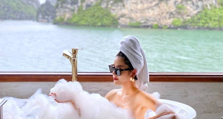 Vrouw ontspant in een schuimbad met uitzicht door het raam op een schilderachtig landschap.