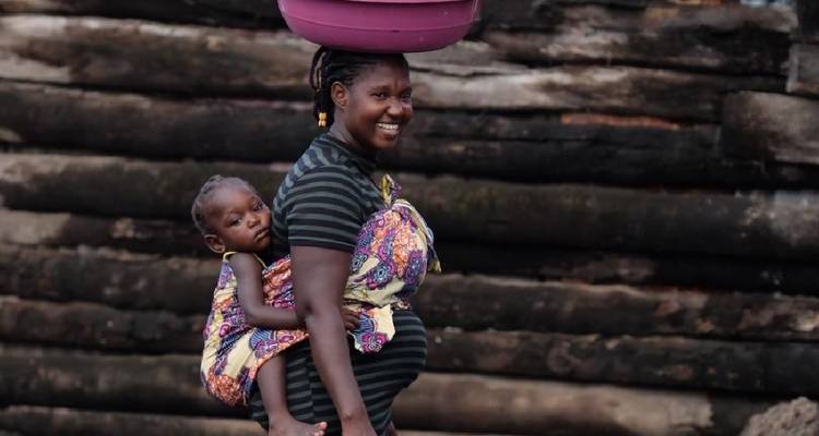 Une femme portant un enfant sur son dos et un panier sur sa tête.