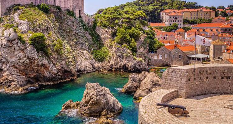 Eaux adriatiques turquoise sous la forteresse perchée sur la falaise de Dubrovnik et les toits de terre cuite.