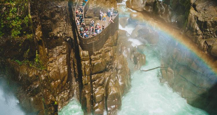 A crowded lookout point with people observing a waterfall and a rainbow.