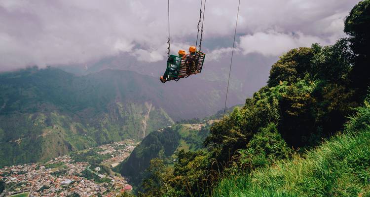 Two people on a swing high above a valley with a view of a town.