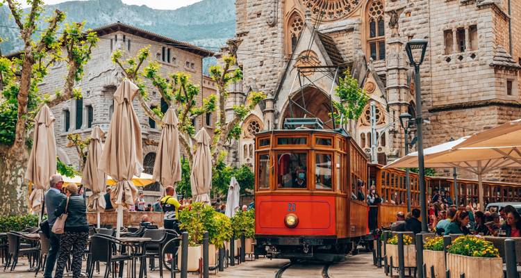 Café en plein air avec des gens, tramway historique et église en arrière-plan.