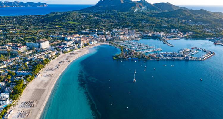 Vue aérienne d'une ville côtière avec plages, marina et montagnes.