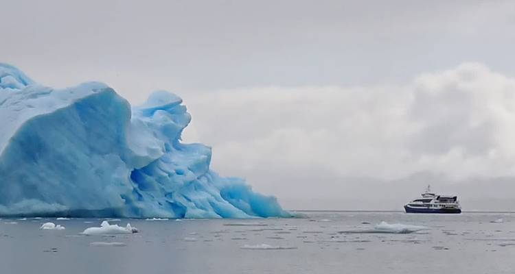 Eisberg treibt im Meer mit einem Boot in der Nähe.
