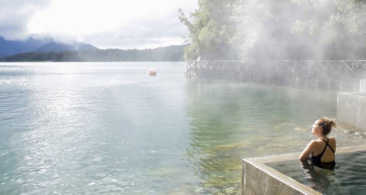 Person entspannt sich in einer heißen Quelle mit Blick auf einen See.
