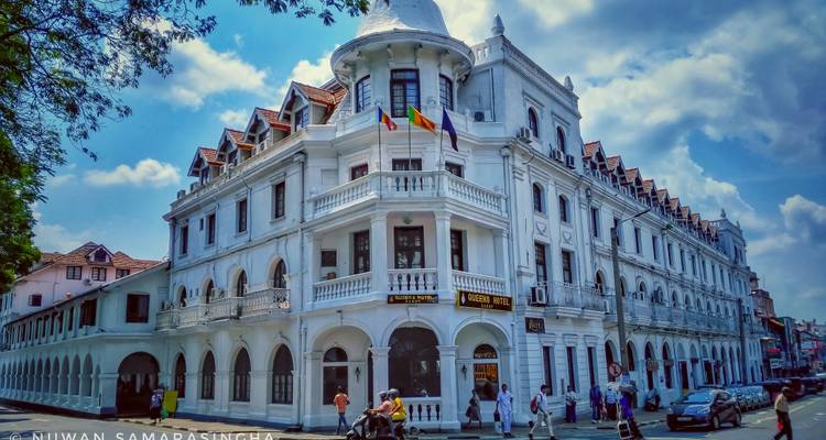 Une vue du bâtiment historique de l'Hôtel Queen dans une rue animée sous un ciel bleu.