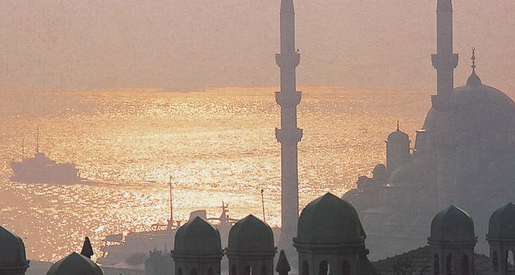Silhouette of mosques against a sunset along a waterway.