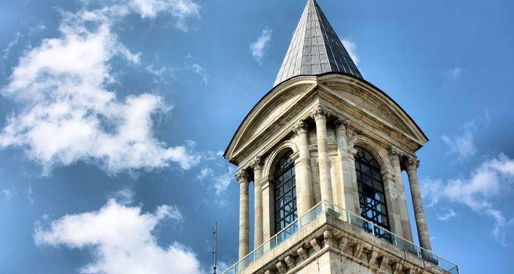 Stone bell tower with pointed roof rising into a clear blue sky, Istanbul architecture detail.