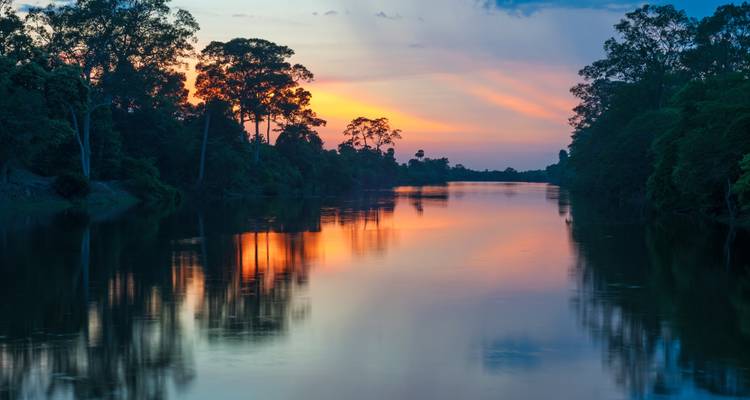 Dramatischer Sonnenuntergangsblick über einen von Bäumen umgebenen Fluss.