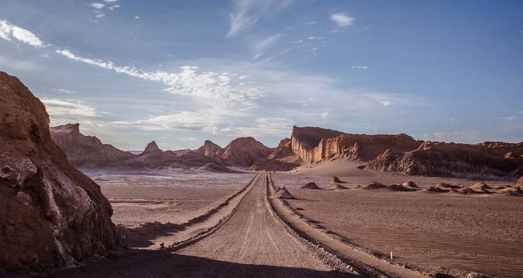 Una carreta de tierra recta corta a través de un dramático valle desértico flanqueado por formaciones dentadas.