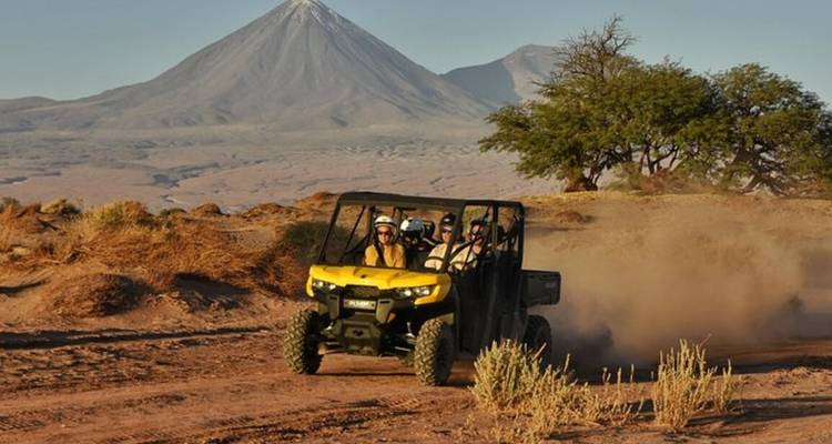 Un vehículo utilitario todoterreno levanta polvo del desierto con un volcán asomándose a lo lejos.