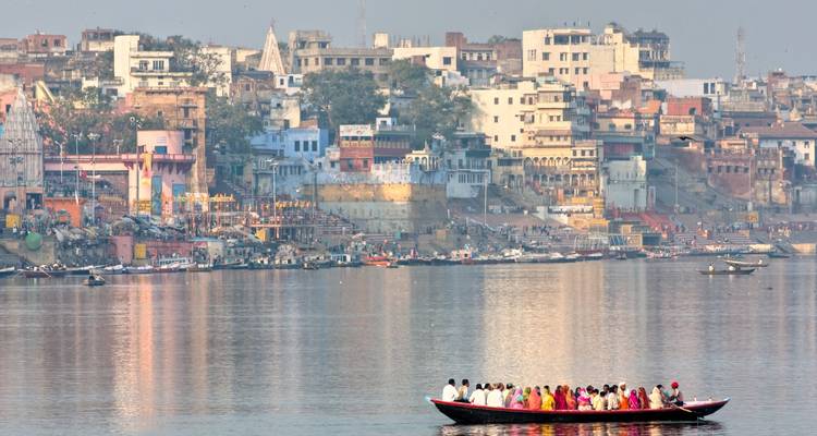 Personas en un barco en el río con los ghats de Varanasi al fondo.